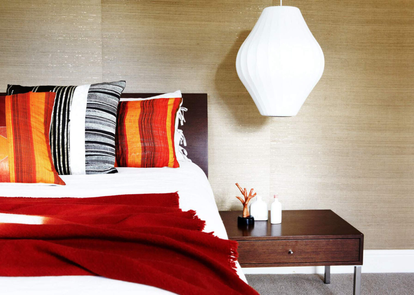 A beautifully styled bedroom featuring a vibrant red blanket, colorful pillows, and a modern pendant light, creating a cozy atmosphere.