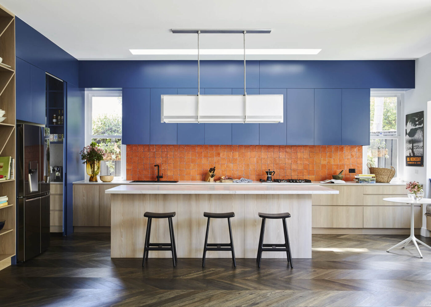 A modern kitchen featuring a stylish design with blue cabinets, an orange tiled backsplash, and a spacious island with three black stools, perfect for inviting gatherings.